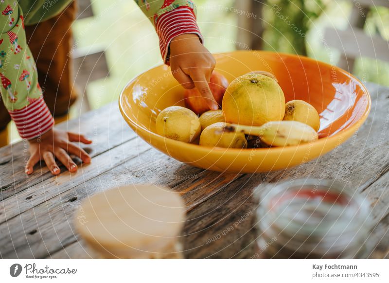 kid's hand pointing to fruits in bowl on table agriculture apple banana children citrus color colorful decorative dessert diet food & drinks fresh glasses hands