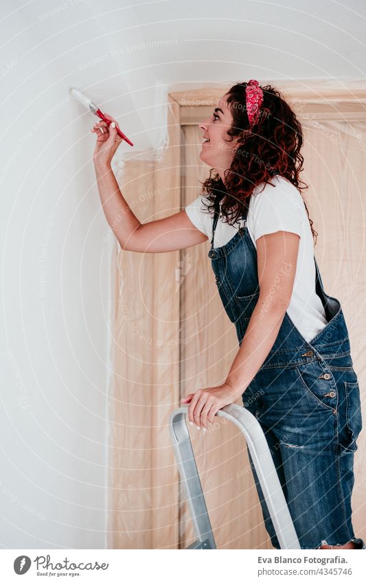 happy caucasian woman painting the room walls with white color. Do it yourself and new home concept house brush young new house painter bricolage solo working