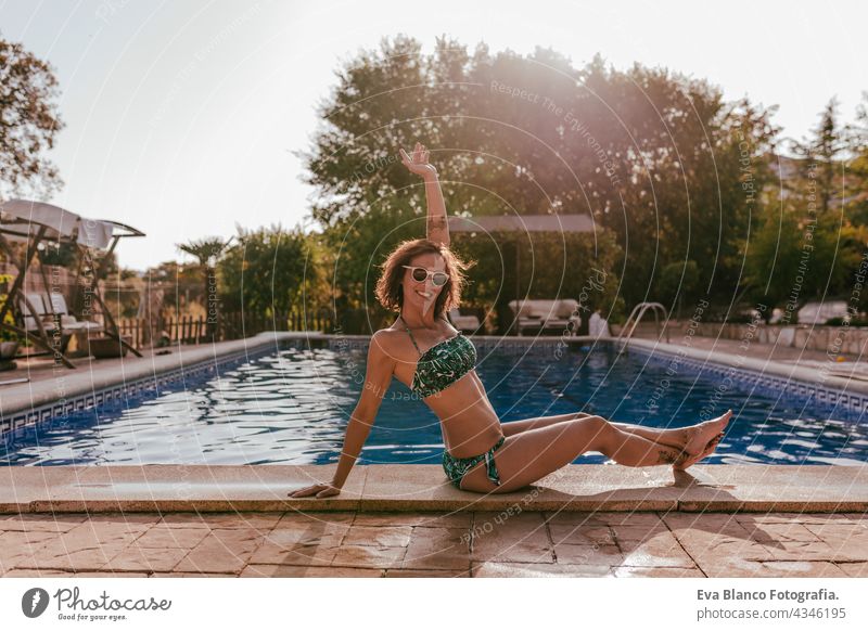 beautiful caucasian woman sitting by pool side wearing bikini swimwear. Summer time, vacation and lifestyle swimming pool sunglasses summer hot funny sunny fit