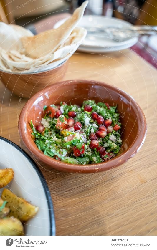 Close-up of a tasty tabbouleh salad with pomegranate seeds in a brown ceramic bowl mezze table snack lebanese food delicious vegetarian vegan sour cream chili