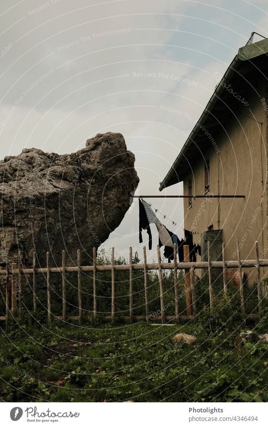 Between the rock and the house is a clothesline with clothes to dry. Fence Garden House (Residential Structure) Laundry garments Meadow Lawn somber Window Roof