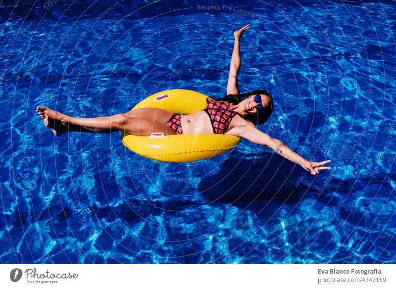 happy caucasian woman floating on yellow donuts inflatable at swimming pool. Summer time, vacation and lifestyle top view summer sunglasses fun beach slim blue