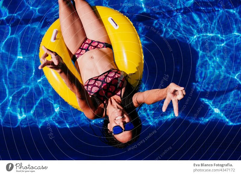 top view of happy caucasian woman relaxing on yellow donuts inflatable at swimming pool. Summer time, vacation and lifestyle floating summer sunglasses fun