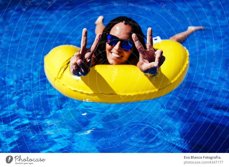 top view of happy caucasian woman relaxing on yellow donuts inflatable at swimming pool. making V sign with hands. Summer time, vacation and lifestyle floating
