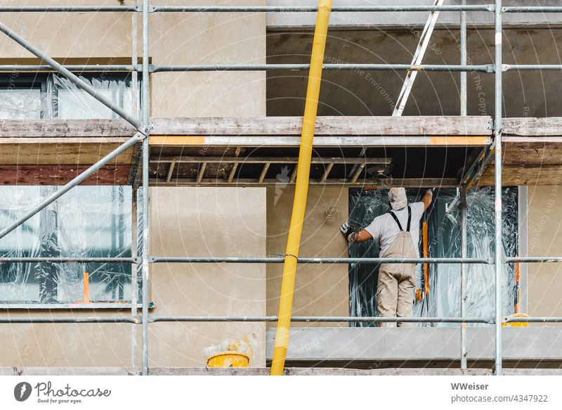 A construction worker tapes the windows with foil, he wants to paint the facade Construction site Construction worker House (Residential Structure)