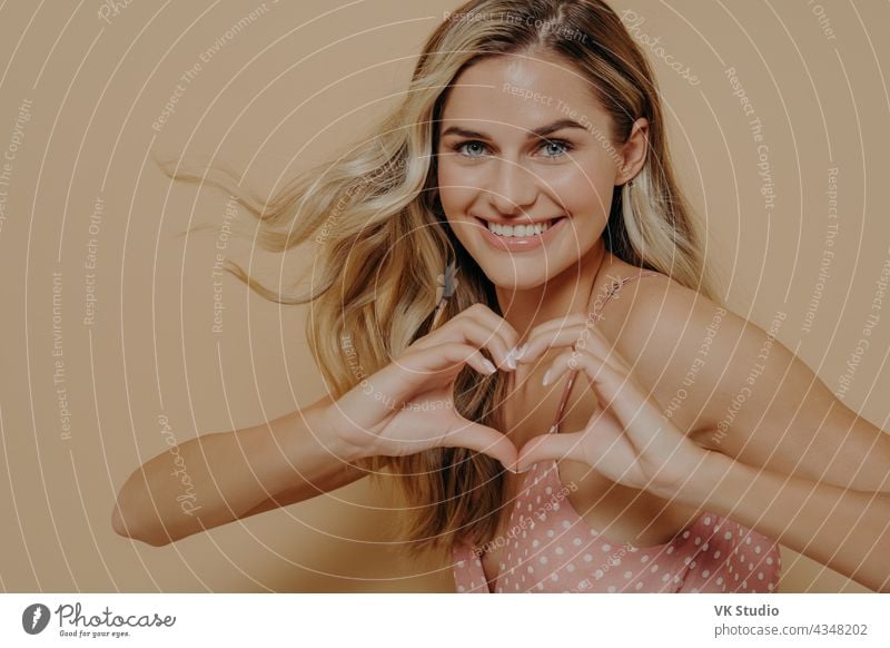 Blonde woman making heart shape with her hands upbeat blonde showing gesture love smile smiling displaying affection tender happy face isolated expression joy