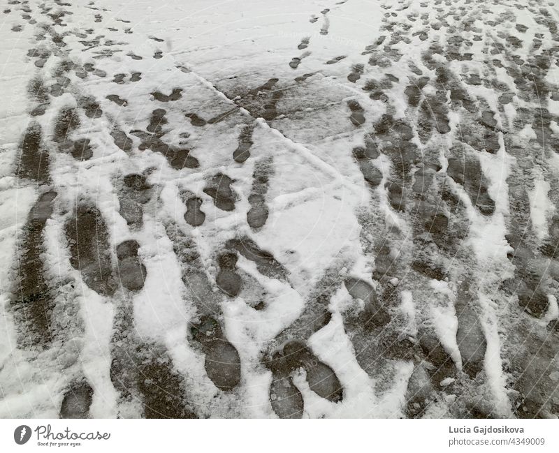 Shoe imprints and dog paws in the snow covered sidewalk close up. The snow has not been cleared away. Slippery ground is risky and dangerous because of potential accident.