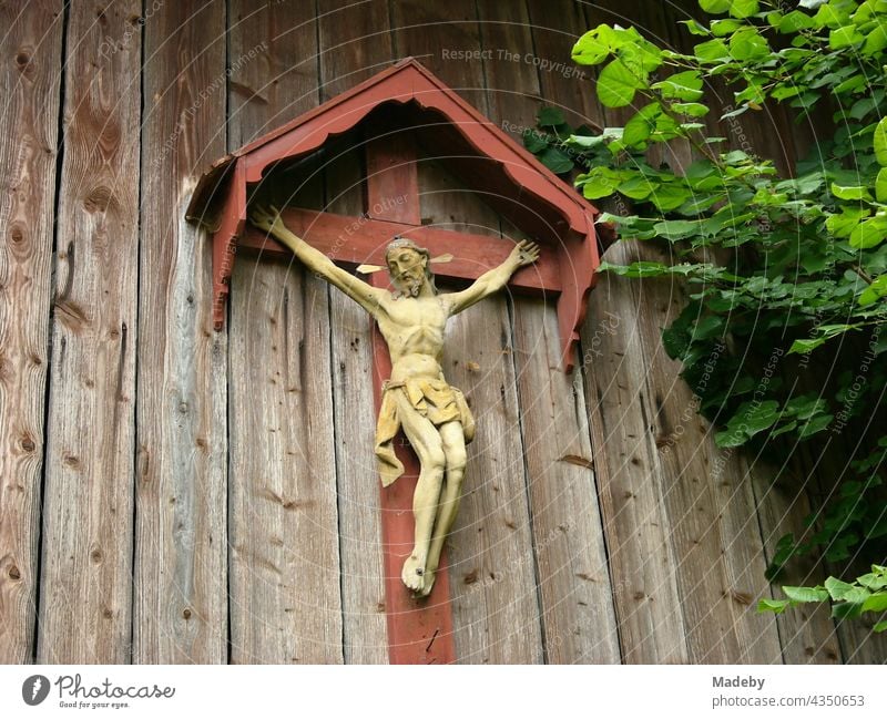 Artful crucifix with Jesus Christ on a roofed cross on the old wood of a barn in Rudersau near Rottenbuch in the district of Weilheim-Schongau in Upper Bavaria