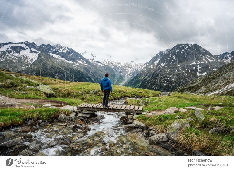 Man hiker resting on small bridge over mountaian river at Schlegeis Lake, Zillertal Alps, Austria zillertal schlegeis austria stausee beautiful lake hiking