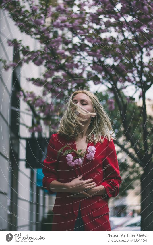 Portrait of a caucasian blonde woman wearing a red formal jacket holding flowers model lifestyle street urban confident nature natural attractive casual Woman