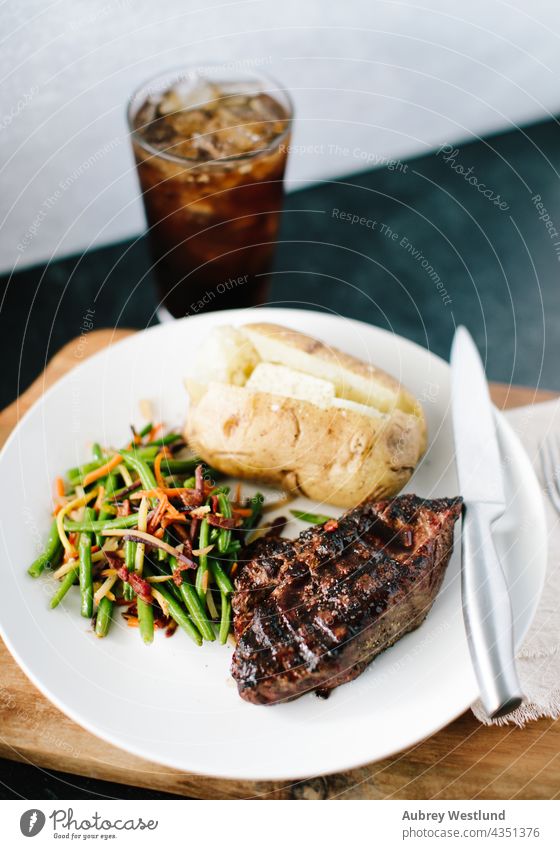 classic steak and potato dinner with a soda on a black and white backdrop angus background baked potato barbecue bbq beef board butcher closeup cooked cooking