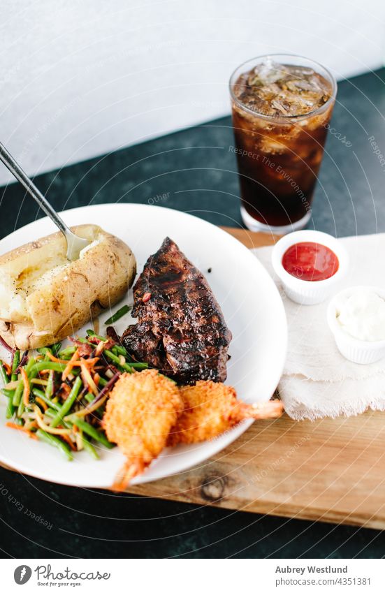 surf and turf steak, prawn and potato dinner with a soda on a black and white backdrop angus background baked potato barbecue beef board breaded butcher closeup