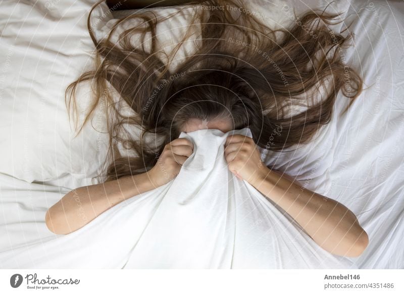 Young woman lying in bed suffering, tired woman covering face with hands, can't sleep feels exhaustand on white sheets in bedroom head ache bedroom closeup