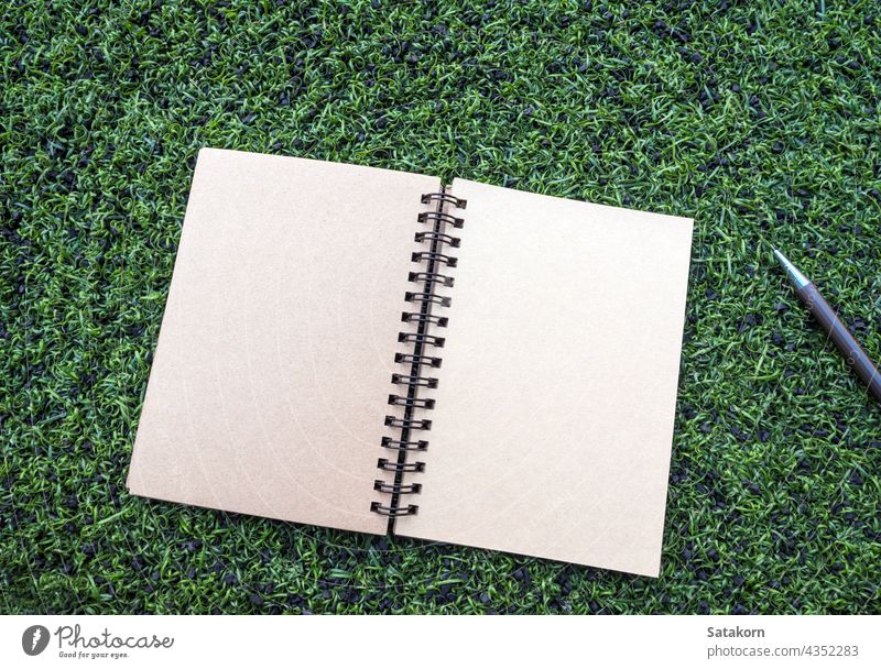 Kraft paper spiral notebook with pen on the Artificial turf blank kraft brown clean empty template page object document pad diary space pencil grass texture