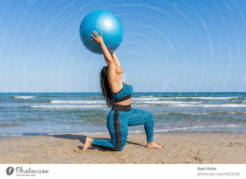 Woman playing with a fitness ball doing sport exercises on beach woman young adult latina afro american yoga plus size health blue lifestyle healthy oversized