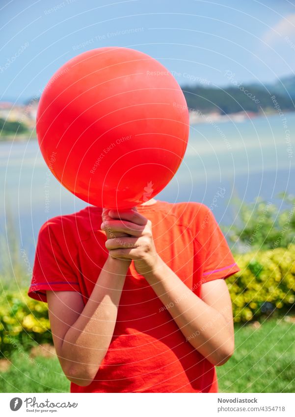 boy hiding face behind a red balloon alone background birthday casual casual clothes caucasian celebrate celebration child childhood colorful cover decorating