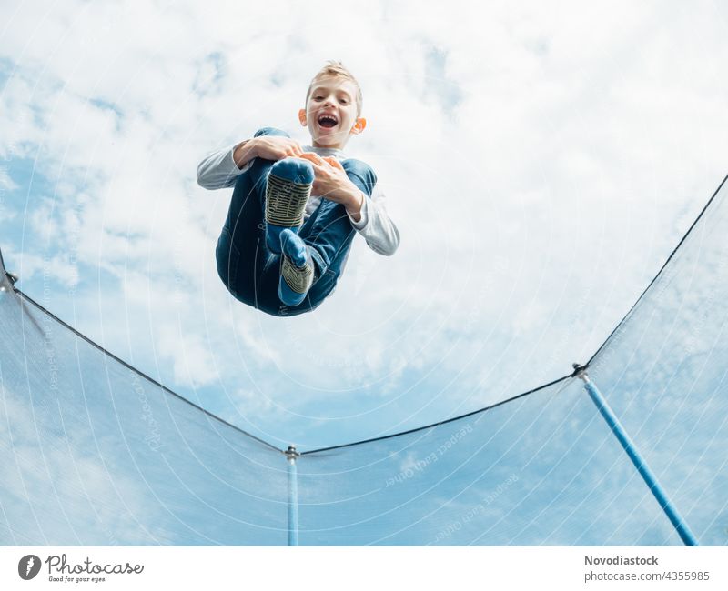 young boy jumping on trampoline male child alone 1 high outdoors smile enjoy happy action motion movement model casual healthy lifestyle jeans caucasian funny