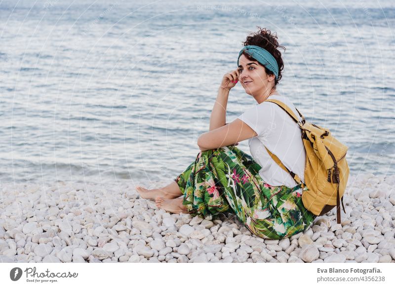 side view of relaxed caucasian woman with yellow backpack sitting at the beach during sunset. summer time. daydreaming. Outdoors lifestyle ocean sea holidays