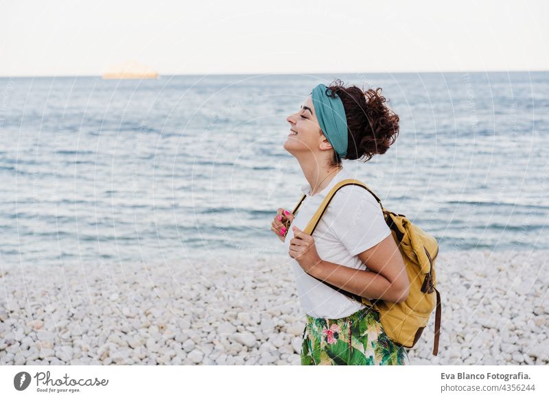relaxed caucasian woman with yellow backpack walking by the beach during sunset. summer time. daydreaming. Outdoors lifestyle ocean sea holidays vacation