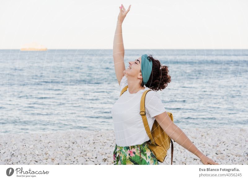 happy caucasian woman with yellow backpack and arms raised at the beach during sunset. summer time. daydreaming. Outdoors lifestyle relax ocean sea holidays
