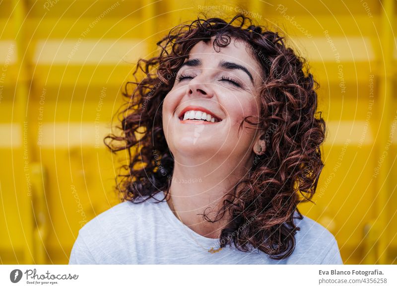 close up of happy caucasian woman with curly hair over yellow background. summer time. Outdoors lifestyle brunette smiling outdoors city carefree smile town