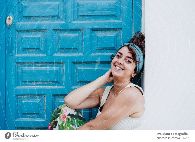 smiling caucasian woman sitting in front of blue door during summer time. Outdoors lifestyle happy outdoors city beach carefree smile town alicante spain