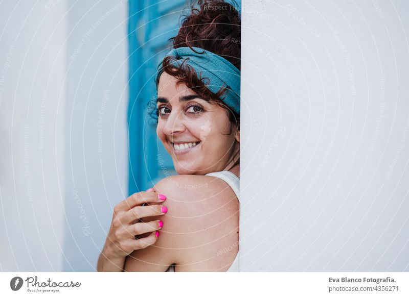 portrait of smiling caucasian woman sitting in front of blue door during summer time. Outdoors lifestyle happy outdoors city beach carefree smile town alicante