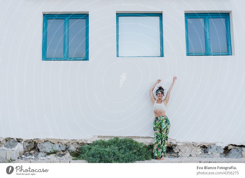 portrait of happy caucasian woman with arms raised in front of blue windows and white wall during summer time. Outdoors lifestyle outdoors city beach carefree