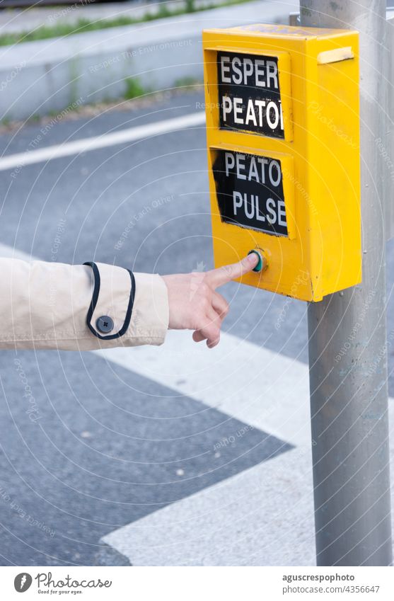 Woman's finger pressing the pedestrian button of a traffic light. The words that appear mean: "wait pedestrian", "press pedestrian". vertical index index finger