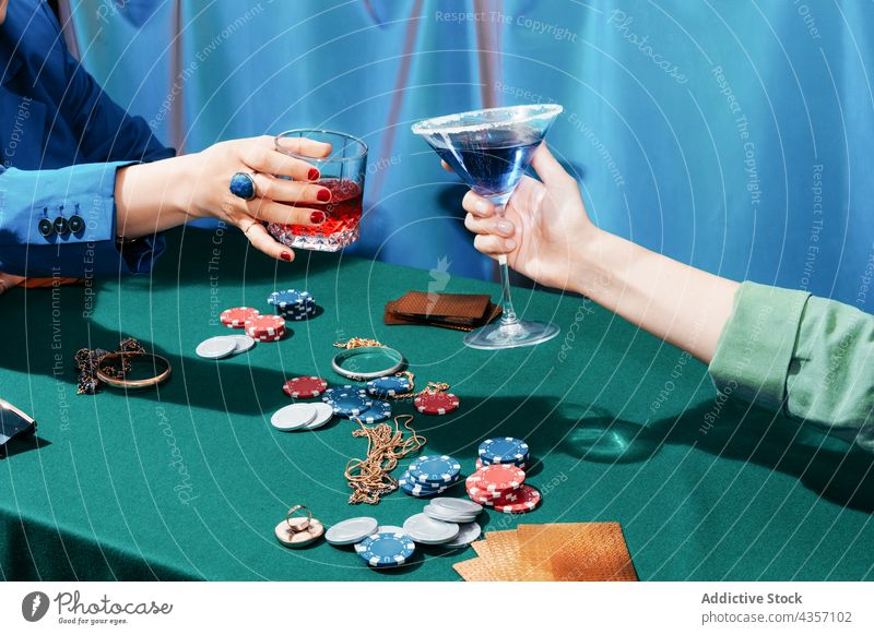 Crop women clinking glasses during poker game cheers gamble play entertain cocktail female friend bet card chip together table sit toast green alcohol drink