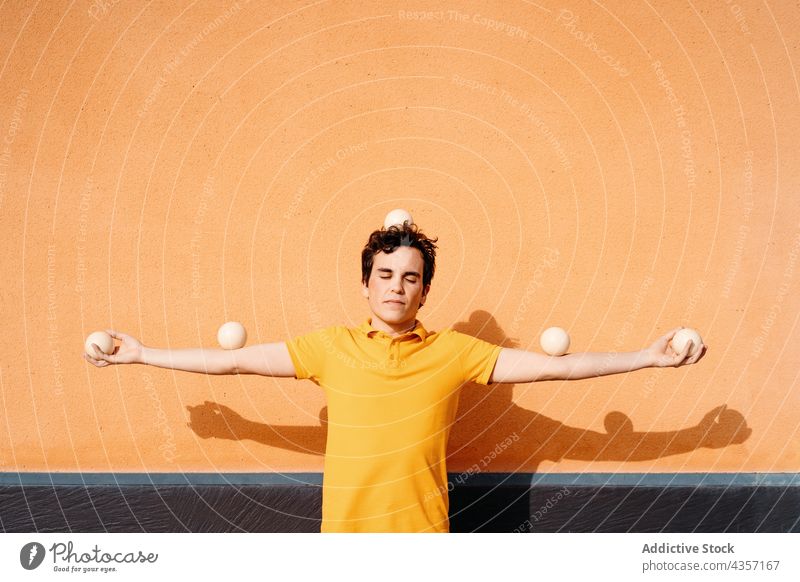 Calm young man with juggling balls standing near wall juggle balance immobile tranquil color calm motionless skill still trick male yellow orange colorful