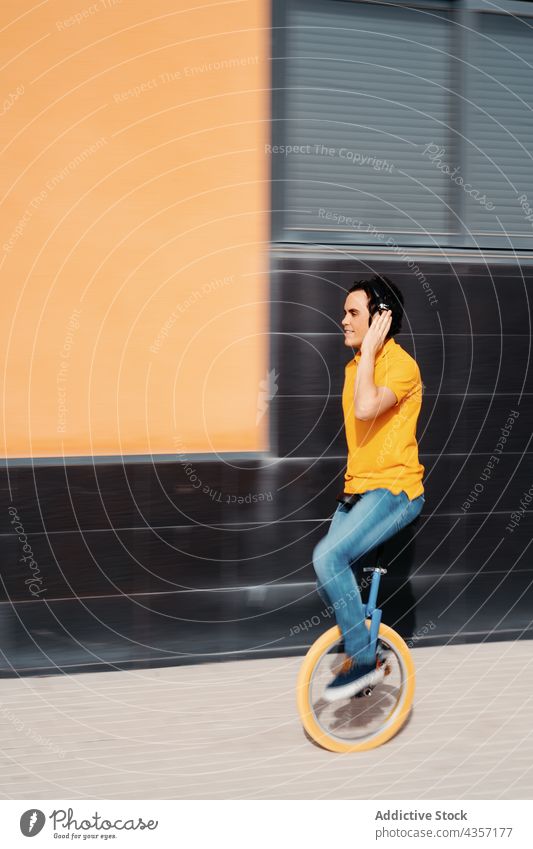 Young man in headphones riding unicycle ride listen urban color modern gadget orange male music device style lifestyle using wheel vehicle transport alternative