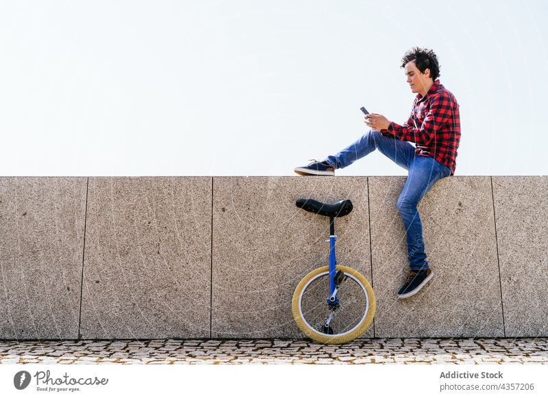 Young man with unicycle using smartphone on street urban modern mobile online gadget male young wheel surfing communicate cellphone free time millennial hipster