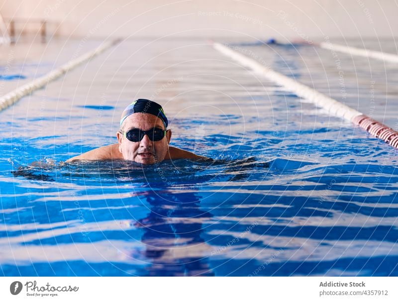 Mature man swimming in pool water aerobic swimmer exercise training activity mature male aqua workout wellbeing vitality wellness glasses cap sport energy