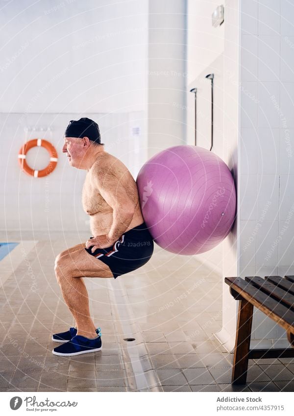 Mature man doing exercise with fitness ball in pool aerobic fit ball training mature squat male middle age water aqua sport activity workout poolside wellbeing