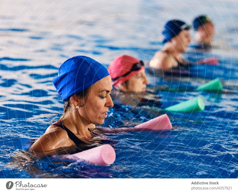 Company of people doing exercise with aqua noodles in pool water aerobic training group activity swim sport foam workout wellbeing vitality wellness equipment