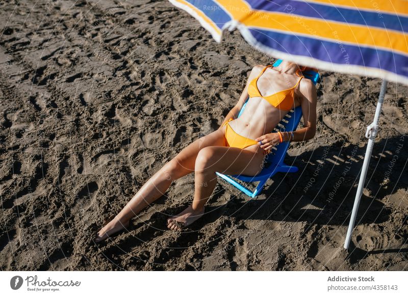 Anonymous woman sitting on beach bikini fit summer vacation beach umbrella sea travel holiday pale anonymous young redhead slim orange female water chair sand