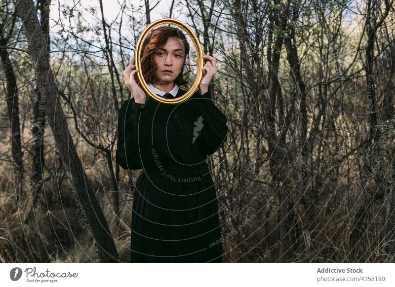 Woman in black dress looking at camera through wooden frame woman unemotional halloween forest autumn holiday female emotionless style mystery woods fall season