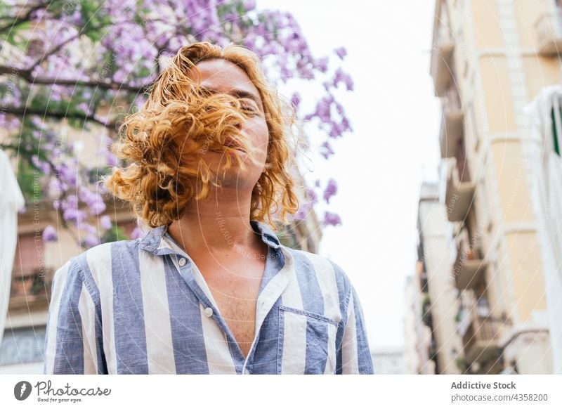 Carefree man with long hair in city flying hair carefree dreamy street summer appearance serene tender male urban curious flower hairstyle daydream pleasure