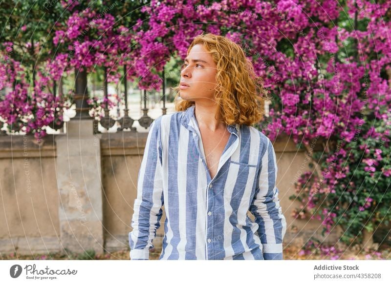 Carefree man with long hair in garden with blooming trees carefree dreamy street summer appearance serene tender male urban curious flower hairstyle daydream