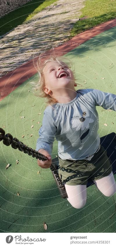 Girl swinging with laugh and joy kid girl child fun toddler people playground playful outdoor funny little small childhood carefree careless vertical freedom