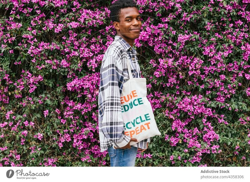 Content black man standing with eco friendly textile bag in garden shopping bag zero waste natural ecology flower male ethnic african american summer happy