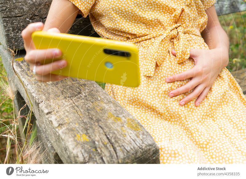 Anonymous pregnant woman taking selfie on smartphone in countryside self portrait touch belly summer tummy female sit rest dress mother expect device enjoy