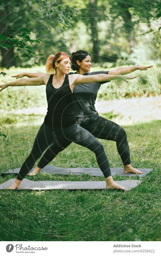 Young sportive women practicing Virabhadrasana B yoga pose in green park warrior ii virabhadrasana b together mindfulness wellness concentrate stress relief
