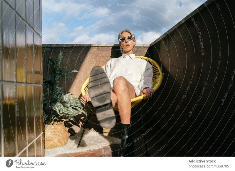 Stylish transgender woman sitting in armchair on terrace style trendy confident queer lgbt fashion outfit female relax modern rest reach out outstretch