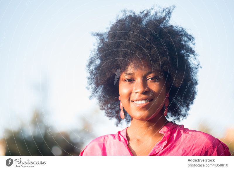 Cheerful black woman with Afro hairstyle standing in park afro charming cheerful smile summer beauty natural female african american ethnic sunny appearance