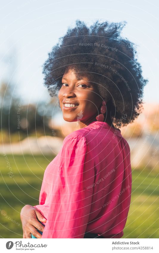 Cheerful black woman with Afro hairstyle standing in park afro charming cheerful smile summer beauty natural female african american ethnic sunny appearance