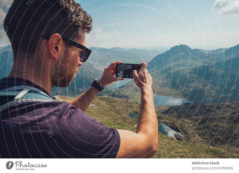 Traveling man taking picture of mountains on smartphone on sunny day traveler take photo hiker highland rocky moment male wales united kingdom uk great britain