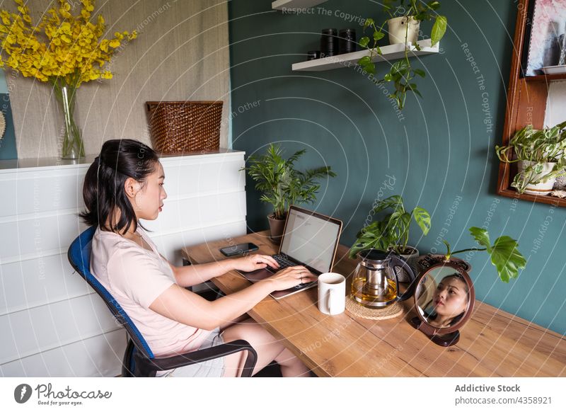 Asian woman reading document on laptop and working at home freelance computer female asian ethnic netbook job cup online using remote device workplace sit table