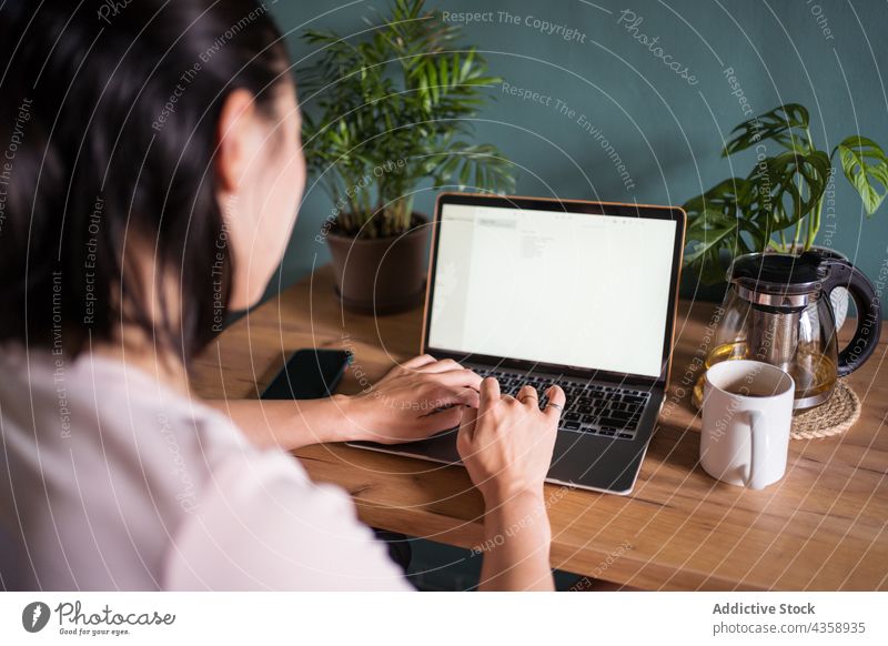 Anonymous Asian woman reading document on laptop and working at home freelance computer female asian ethnic netbook job cup online using remote device workplace